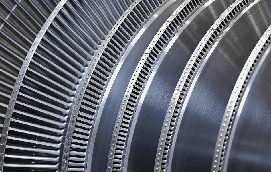 Nahaufnahme von mehreren metallenen Turbinenschaufeln, die spiralförmig angeordnet sind. Die Oberfläche ist glänzend und zeigt feine Rillen sowie präzise Befestigungsdetails. Die Struktur deutet auf eine komplexe technische Konstruktion hin.