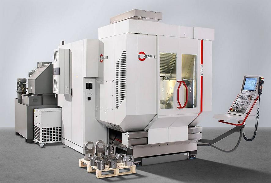 Eine moderne CNC-Maschine in einem industriellen Umfeld. Die Maschine hat eine große, weiße Gehäusekonstruktion mit Fenster, einem Bedienfeld und einem Stapel von bearbeiteten Metallteilen davor. Im Hintergrund ist eine weitere Maschine sichtbar.